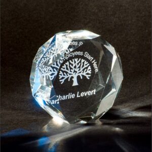 Clear crystal trophy with engraved tree graphic and text for employee recognition, displayed on a dark surface.