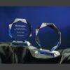 Octavia crystal trophy awards with faceted edges, one engraved for corporate recognition, on black fabric with blue backdrop.