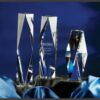 Clear crystal trophy awards with faceted edges on satin fabric; one engraved, ideal for corporate or employee recognition.