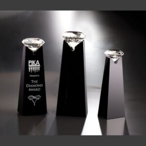 Black crystal trophy pedestals with solitaire crystal awards, tallest engraved "PIKA Presents The Diamond Award" for recognition.