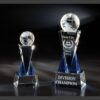 Crystal globe trophies with blue accents on a reflective surface, featuring a corporate champion crystal award.