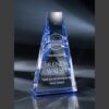 Blue crystal pyramid trophy recognizing dedicated service, displayed on a reflective base against a dark background.
