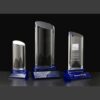 Crystal award trophies with blue bases, tallest in center, right trophy engraved for corporate recognition.