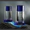 Cylindrical crystal trophies with blue bases for corporate recognition, shown engraved and blank, displayed on draped fabric.