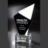 Crystal glass trophy engraved with "Health Hero" honoring Dr. Gray Bentley, corporate recognition award on dark background.
